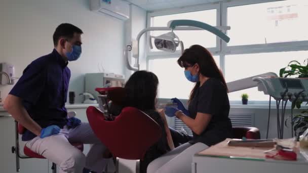 Врачи-стоматологи Женщина и мужчина в медицинских масках обслуживают пациента в стоматологической клинике - Кадры, видео