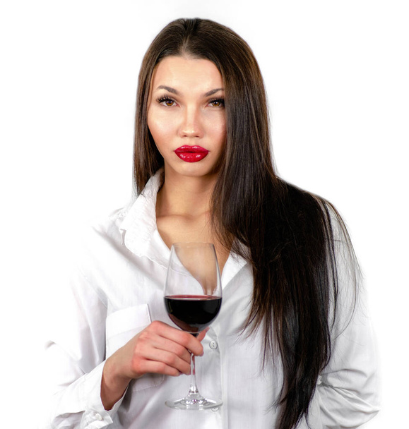 Csinos arc barna lány érzéki megjelenés és hosszú haj és nagy ajkak kezében üveg vörösbor fehér háttér. - Fotó, kép