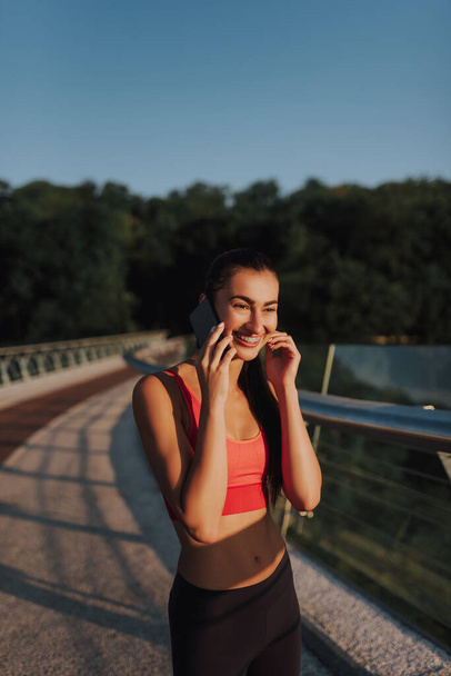 Beautiful girl is talking on her phone. Woman healthy lifestyle outdoor. Phoning after a morning run - Photo, Image