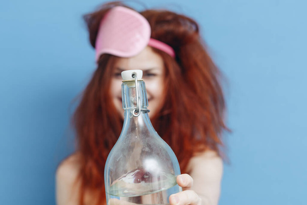 donna allegra con capelli spettinati e bottiglia di alcool maschera di sonno vacanza - Foto, immagini