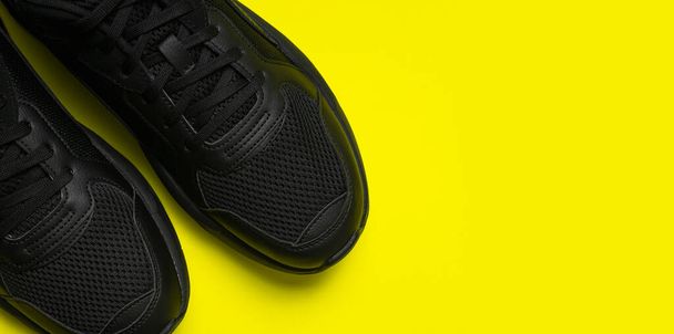 Black classic men's sneakers on bright yellow background. Fashionable youth sports sneakers. Sports casual shoes. Footwear for fitness, running, healthy lifestyle. Flat lay top view copy space. - Photo, Image
