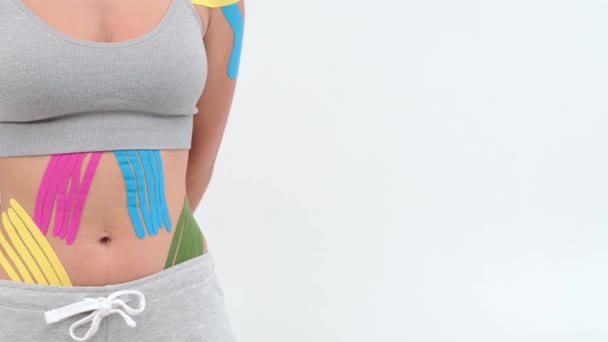 Kinesiology tape on girl belly. body with kinesio tape on the abdomen of young girl. Sport tratment rehabilitation. Copy space on light background - Footage, Video