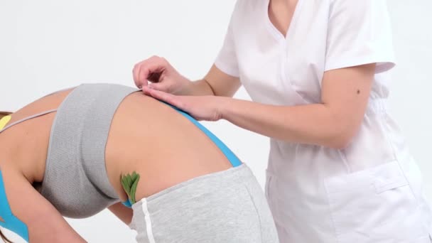 Fysiotherapeut plakt kinesio tapes aan de kleine rug van vrouwelijke patiënt, kinesiologie taping, kinesiologische therapie, atleet herstellen na letsel aan de lendenen. professionele lijm tapes langs de wervelkolom - Video