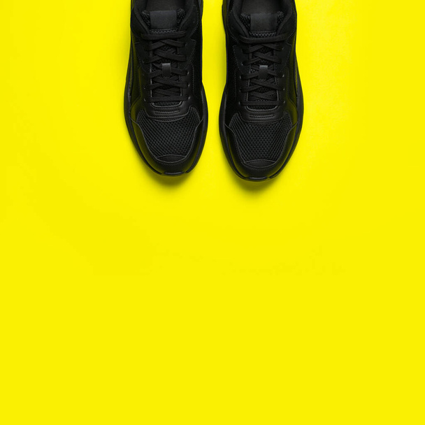 Sneakers classiche da uomo nere su sfondo giallo brillante. Scarpe da ginnastica sportive giovanili alla moda. Scarpe sportive casual. Calzature per fitness, corsa, stile di vita sano. Posa piatta vista dall'alto copia spazio. - Foto, immagini
