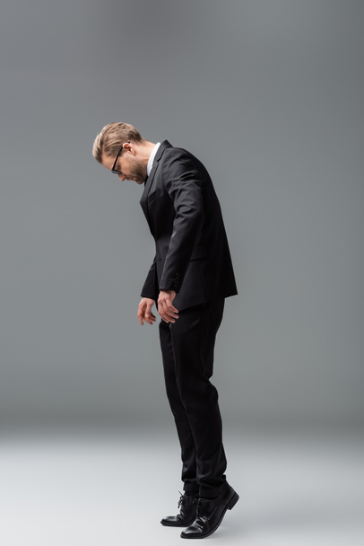 Вид в полный рост бизнесмена в черном костюме, стоящего на кончике пальца на сером - Фото, изображение