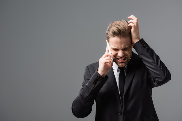 stresszes menedzser beszél a mobiltelefon és megérinti fej elszigetelt szürke - Fotó, kép