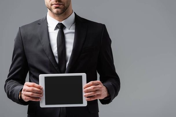 vista recortada del gerente en traje negro sosteniendo tableta digital con pantalla en blanco aislado en gris - Foto, imagen