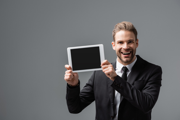 alegre gerente corporativo mostrando tableta digital con pantalla en blanco aislado en gris - Foto, Imagen