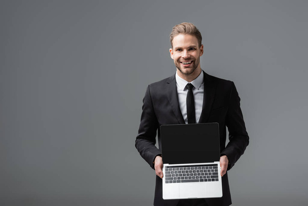 vreugdevolle manager met laptop met blanco scherm geïsoleerd op grijs - Foto, afbeelding