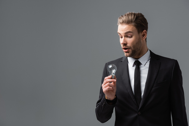 erstaunt Manager im Anzug hält Glühbirne isoliert auf grau - Foto, Bild