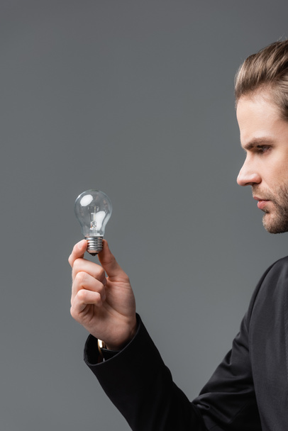 молодий бізнесмен тримає лампочку ізольовано на сірому
 - Фото, зображення