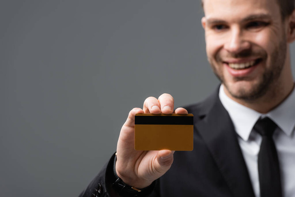 empresário feliz mostrando cartão de crédito em fundo borrado isolado em cinza - Foto, Imagem