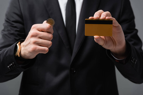 částečný pohled na obchodníka zobrazující kreditní karty a mince na rozmazaném pozadí izolované na šedé - Fotografie, Obrázek