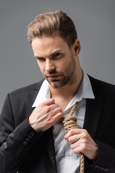 depressed businessman looking at camera while touching rope on neck isolated on grey - Photo, Image