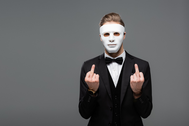 επιχειρηματίας που δείχνει μεσαία δάχτυλα φορώντας μάσκα προσώπου απομονωμένη σε γκρι - Φωτογραφία, εικόνα