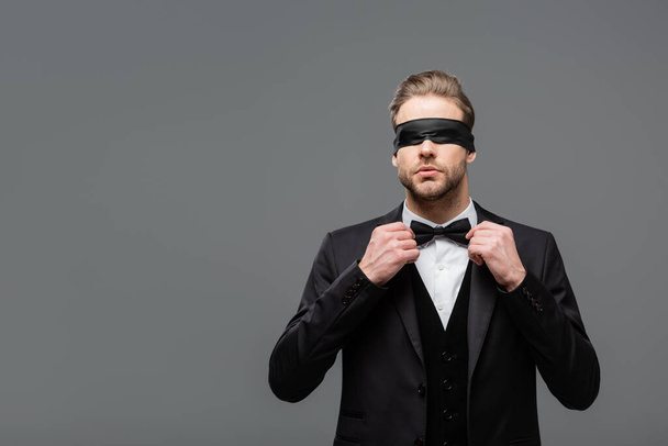 elegant, blindfolded businessman adjusting bow tie isolated on grey - Photo, Image