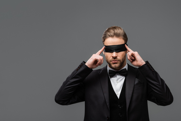элегантный бизнесмен регулируя повязку на глаза изолированы на серый - Фото, изображение