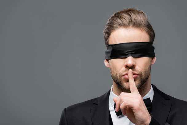 Geschäftsmann mit Augenbinde zeigt Schweigezeichen auf Grau - Foto, Bild