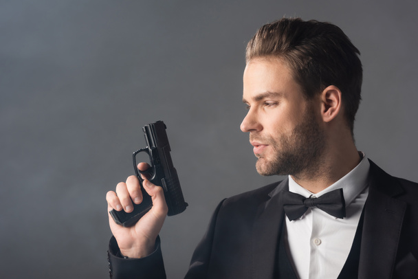 νεαρός επιχειρηματίας με αυτοπεποίθηση κρατώντας όπλο σε γκρι φόντο με καπνό - Φωτογραφία, εικόνα