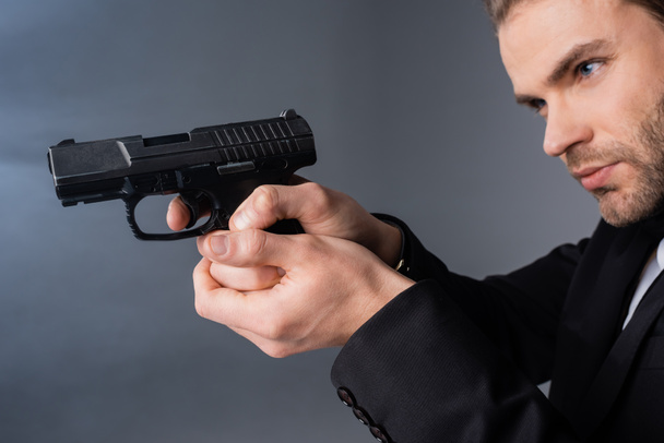 young businessman aiming with gun on grey background with smoke - Photo, Image