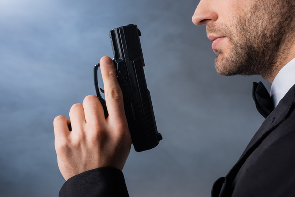 Ausgeschnittene Ansicht eines jungen Geschäftsmannes mit Pistole auf grauem Hintergrund mit Rauch - Foto, Bild