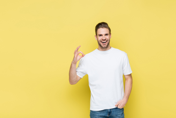 excited man holding hand in pocket and showing okay symbol on yellow - Photo, Image