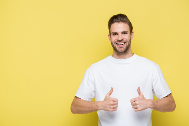 pleased man smiling at camera and showing thumbs up on yellow - Photo, Image