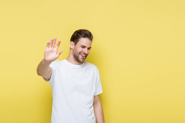 hombre alegre con los ojos cerrados mostrando gesto de basura en amarillo - Foto, Imagen