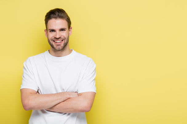 happy man smiling at camera while standing with crossed arms on yellow - Photo, Image