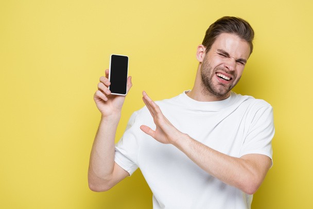 férfi érzés undor és mutató elutasító gesztus, miközben a mobiltelefon üres képernyőn sárga - Fotó, kép