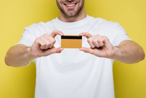 cropped view of smiling man showing credit card on yellow, blurred background - Photo, Image