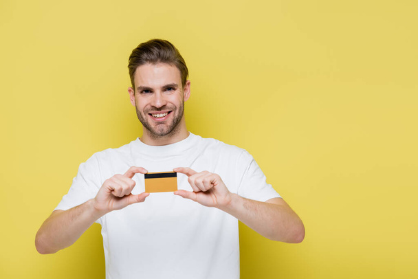 fröhlicher Mann lächelt in die Kamera, während er seine Kreditkarte auf gelb zeigt - Foto, Bild