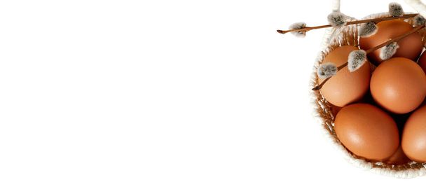 banner. weißer Hintergrund mit handgemachtem Strohkorb voller Eier, Pussy Weidenzweig. Kopierraum. leere Textstelle. Osterferienkarte. Frühjahrsmockup-Design. gesunde ernährung. landwirtschaftliche Produktion. - Foto, Bild