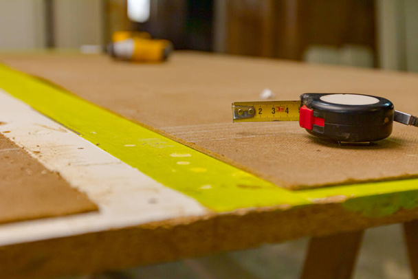Fita de medição para medição é colocada na madeira compensada em oficina de carpintaria. - Foto, Imagem