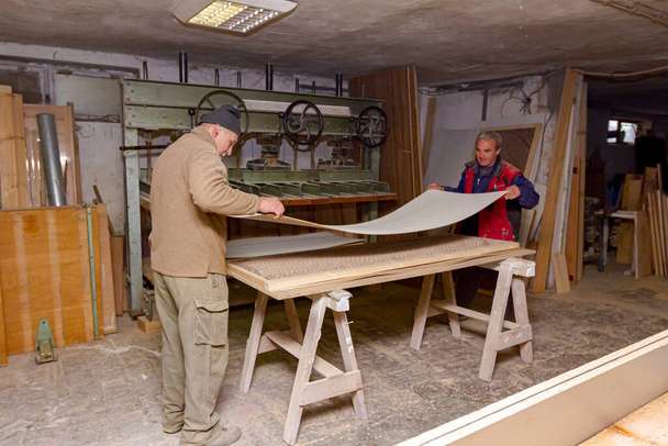 Les menuisiers assemblent des profilés en bois enduits de colle et les préparent à serrer dans la presse à bois à l'atelier de menuiserie. - Photo, image