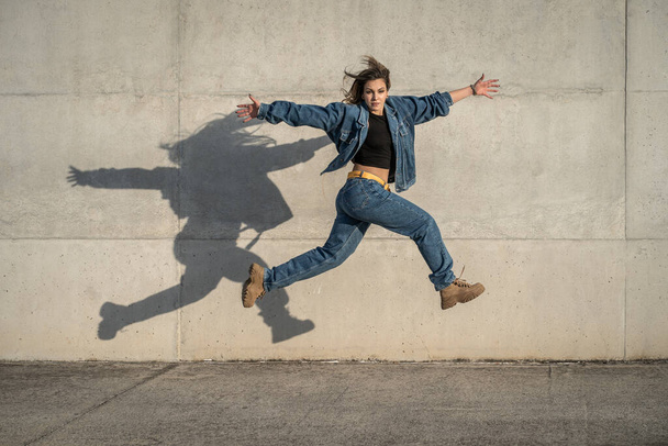 Молодая танцовщица прыгает на сером фоне и отражает тень. Горизонтальная фотография - Фото, изображение