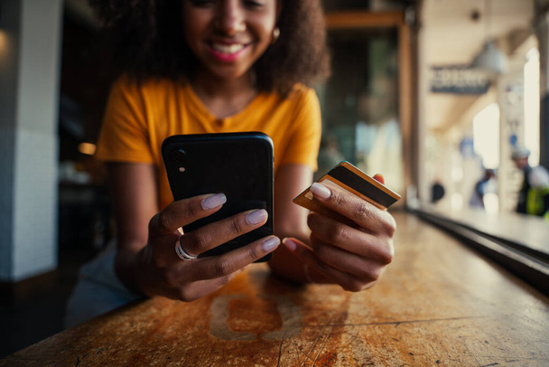 close-up de mensagens de texto feminino de raça mista no smartphone segurando cartão de crédito pronto para fazer o pagamento no café  - Foto, Imagem