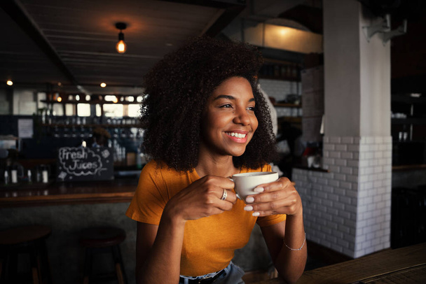 bela fêmea étnica sorrindo enquanto bebe café no restaurante rústico - Foto, Imagem