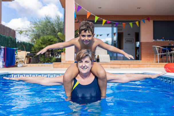 Grandmother carrying his grandson on his shoulders in a swimming pool - Photo, Image