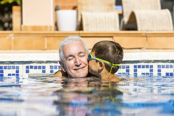 Grandson kissing his grandpa on a swimming pool - Photo, Image
