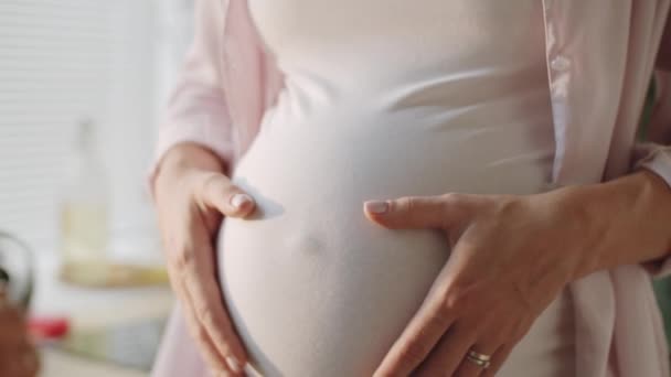 Zbliżenie pochylenie w dół strzał nierozpoznawalnej kobiety w ciąży czule głaskanie jej brzuch i trzymanie się za ręce w kształcie serca - Materiał filmowy, wideo