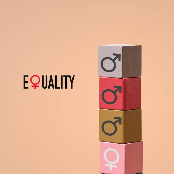 a palavra igualdade e uma pilha de blocos de construção de cores diferentes com símbolos de gênero masculino pintados sobre eles e um bloco de construção com um símbolo de gênero feminino na base, em um fundo marrom - Foto, Imagem