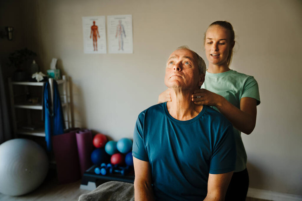 женщина-физиотерапевт проводит тест шеи пожилого мужчины - Фото, изображение
