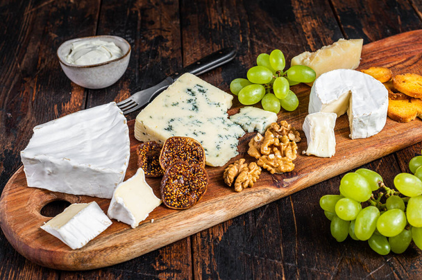 Ποικιλία τυριών με Brie, Camembert, Roquefort, παρμεζάνα, μπλε τυρί κρέμα, σταφύλι και ξηρούς καρπούς. Σκούρο ξύλινο φόντο. Άνω όψη - Φωτογραφία, εικόνα