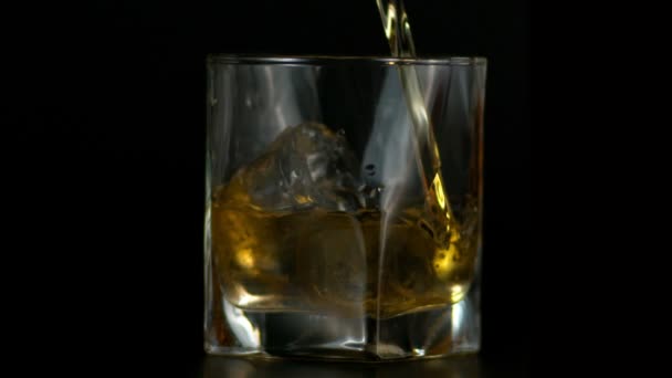Slow Motion di versare whisky in vetro con ghiaccio in fondo scuro  - Filmati, video