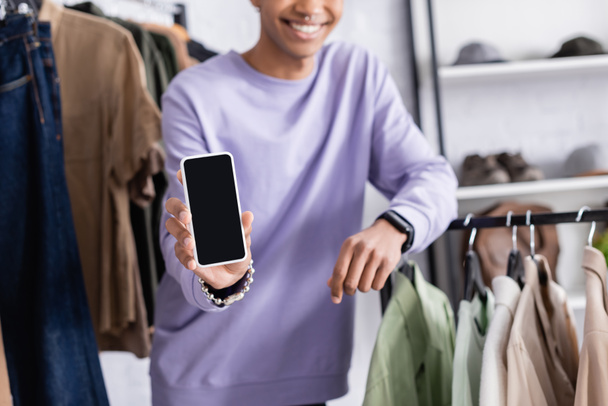 Oříznutý pohled na smartphone v ruce s úsměvem africký americký majitel showroomu na rozmazaném pozadí  - Fotografie, Obrázek