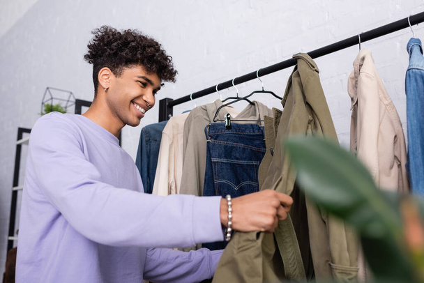 alegre afroamericano showroom propietario mirando ropa en colgante rack  - Foto, imagen