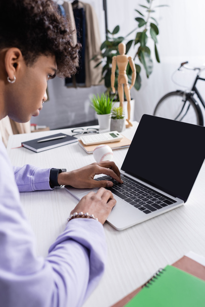 Laptop με λευκή οθόνη κοντά στην αφρικανική Αμερικανός επιχειρηματίας σε θολή πρόσοψη εργασίας σε εκθεσιακό χώρο  - Φωτογραφία, εικόνα