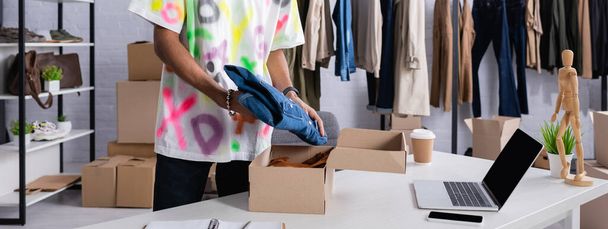 Oříznutý pohled na afrického amerického drobného podnikatele, jak dává oblečení do kartonové krabice v showroomu, banner  - Fotografie, Obrázek