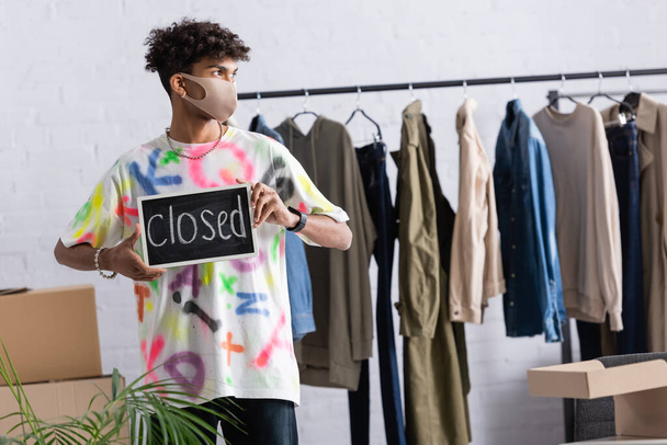 Proprietario di piccole imprese afroamericane in maschera protettiva contenente lavagna con scritte chiuse nello showroom  - Foto, immagini